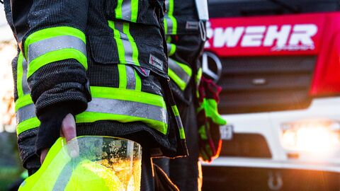 Feuerwehr Feuerwehrmann mit Helm im Vordergrund und ein Feuerwehrauto im Hintergrund.