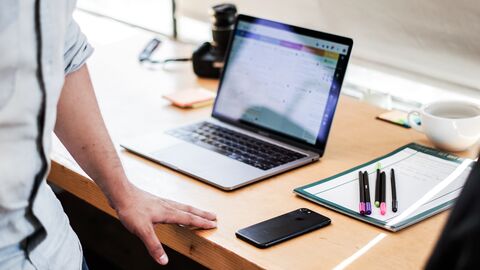 Büroarbeit Ein Laptop und ein Block mit Stiften liegen auf einem Schreibtisch. Davor steht ein Mann, der gerade aus dem Bild läuft.