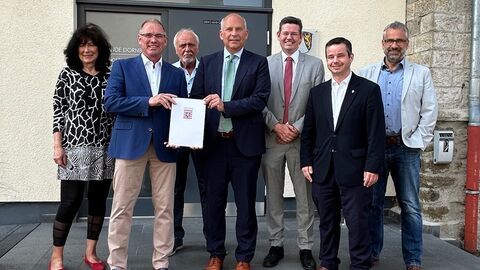 Alle Beteiligten der erste Auszahlung aus Sofortprogramm „Sicherheit bei Veranstaltungen“ stehen vor einem Gebäude mit dem Bescheid in der Hand.